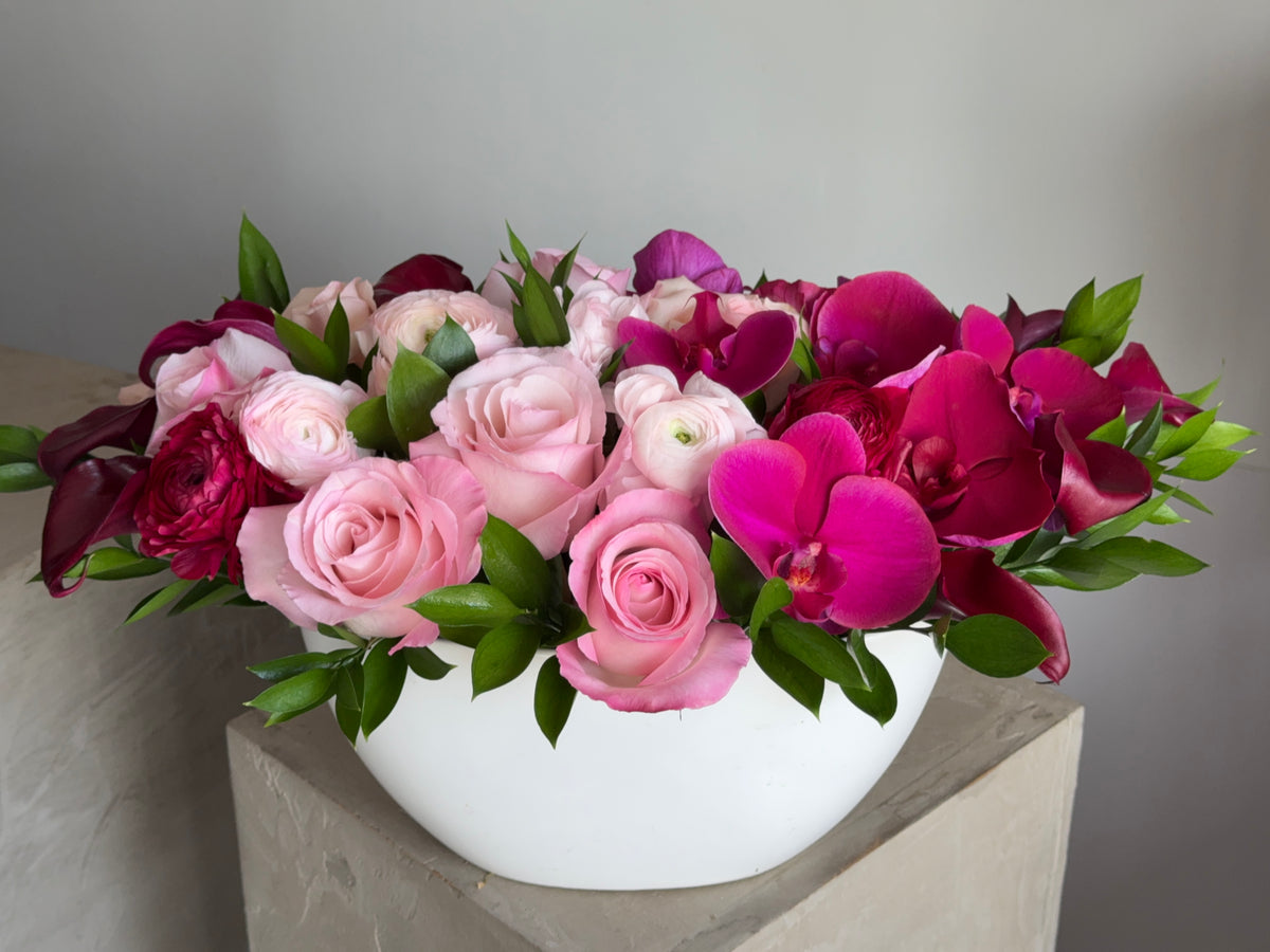 Rose Bordeaux, pink roses, ranunculus, fuchsia orchids and burgundy calla lilies in a white oval vase