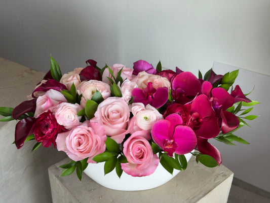 Rose Bordeaux, pink roses, ranunculus, fuchsia orchids and burgundy calla lilies in a white oval vase